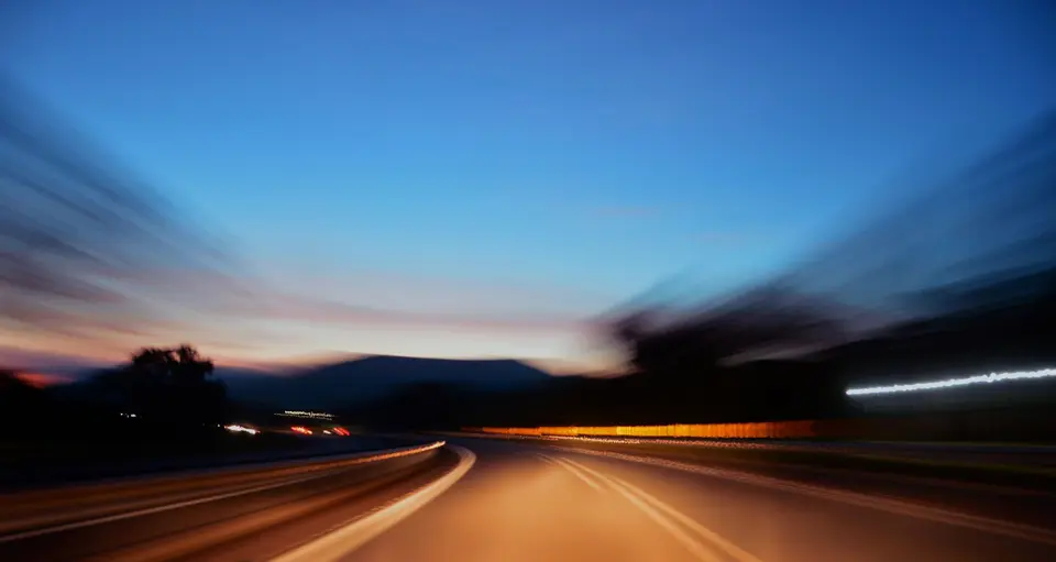 Highway at dusk seen from a moving vehicle, the roadside blurred by speed