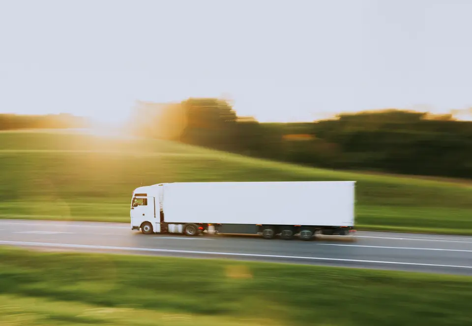 White semi-truck with a plain trailer on a highway, blurred by motion in low evening sun