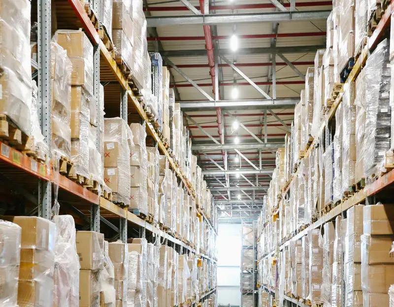 Long warehouse aisle between tall racks of boxes wrapped in plastic